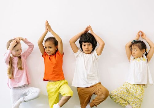 Smiling child performing a simple yoga pose with joy indoors.